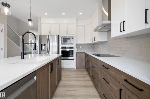 Kitchen featuring brown cabinetry, wall chimney range hood, white cabinetry, stainless steel appliances, and recessed lighting - 4544 Kinsella Link, Edmonton, AB - Indoor Photo Showing Kitchen With Upgraded Kitchen