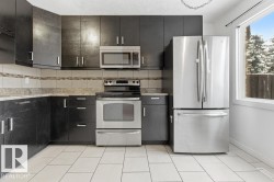 Kitchen featuring stainless steel appliances, dark cabinetry, light tile patterned floors, decorative backsplash, and light stone countertops - 
