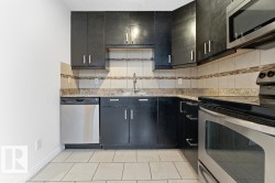 Kitchen with stainless steel appliances, dark cabinetry, tasteful backsplash, light stone countertops, and light tile patterned flooring - 