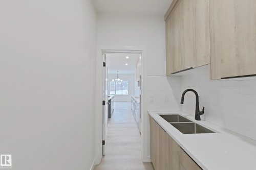 Kitchen with light brown cabinets, modern cabinets, light stone countertops, hanging light fixtures, and a chandelier - 3158 Magpie Way, Edmonton, AB - Indoor Photo Showing Kitchen With Double Sink