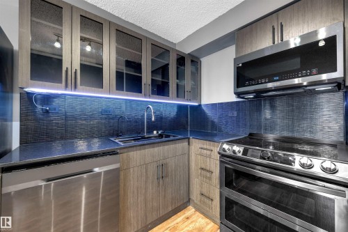 Kitchen with appliances with stainless steel finishes, glass insert cabinets, a textured ceiling, decorative backsplash, and light wood-style flooring - 1702 10150 117 Street, Edmonton, AB - Indoor Photo Showing Kitchen