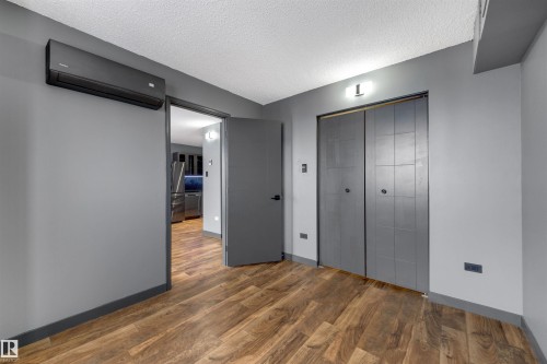Unfurnished bedroom featuring a wall unit AC, a textured ceiling, a closet, wood finished floors, and freestanding refrigerator - 1702 10150 117 Street, Edmonton, AB - Indoor Photo Showing Other Room