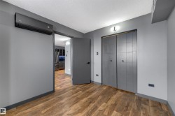 Unfurnished bedroom featuring a wall unit AC, a textured ceiling, a closet, wood finished floors, and freestanding refrigerator - 