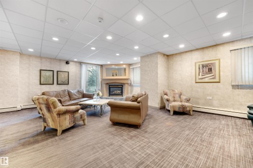 Living area featuring a baseboard heating unit, a glass covered fireplace, recessed lighting, and a drop ceiling - 1702 10150 117 Street, Edmonton, AB - Indoor With Fireplace