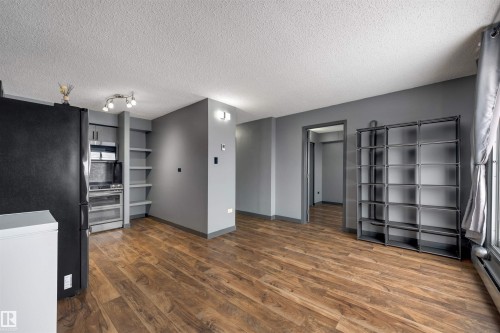 Unfurnished living room featuring a textured ceiling, dark wood finished floors, and baseboard heating - 1702 10150 117 Street, Edmonton, AB - Indoor Photo Showing Other Room