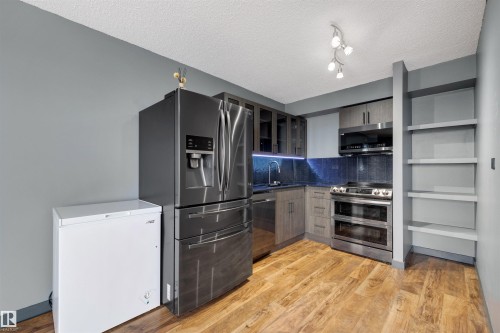 Kitchen featuring appliances with stainless steel finishes, tasteful backsplash, light wood-style floors, dark countertops, and glass insert cabinets - 1702 10150 117 Street, Edmonton, AB - Indoor Photo Showing Kitchen With Stainless Steel Kitchen