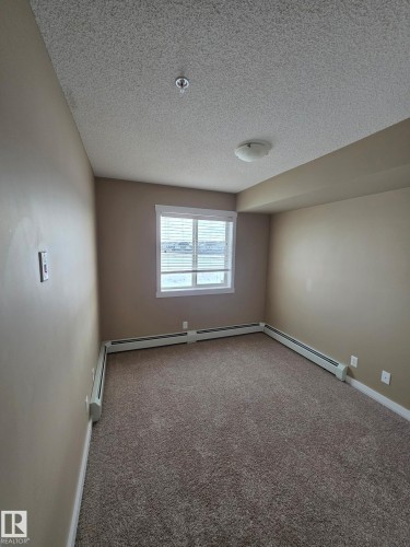 Unfurnished room featuring carpet floors, a textured ceiling, and a baseboard heating unit - 313 1510 Watt Drive, Edmonton, AB - Indoor Photo Showing Other Room