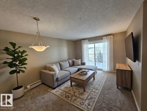 Living room featuring a baseboard radiator, carpet flooring, and a textured ceiling - 313 1510 Watt Drive, Edmonton, AB - Indoor Photo Showing Living Room
