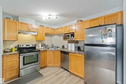 Kitchen with stainless steel appliances, a textured ceiling, under cabinet range hood, light wood-type flooring, and backsplash - 