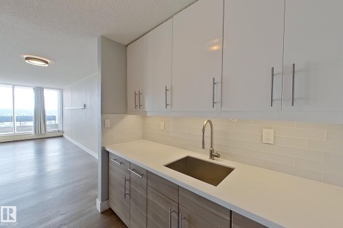 Kitchen featuring a textured ceiling, wood finished floors, modern cabinets, light stone counters, and backsplash - 133 8735 165 Street, Edmonton, AB - Indoor Photo Showing Kitchen