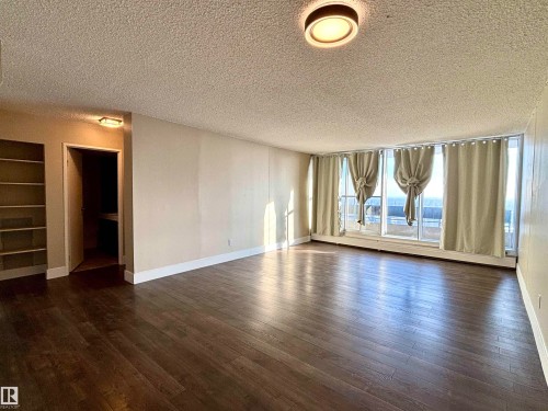 Empty room with a textured ceiling, dark wood finished floors, and a baseboard radiator - 133 8735 165 Street, Edmonton, AB - Indoor