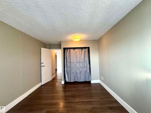 Unfurnished bedroom with dark wood-type flooring, a textured ceiling, and a closet - 133 8735 165 Street, Edmonton, AB - Indoor Photo Showing Other Room