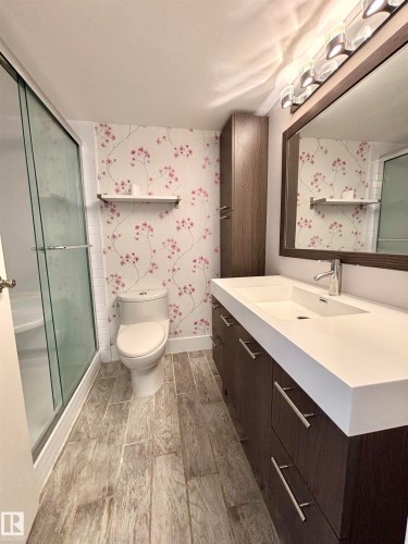Bathroom with a shower stall, wallpapered walls, vanity, and wood finish floors - 133 8735 165 Street, Edmonton, AB - Indoor Photo Showing Bathroom