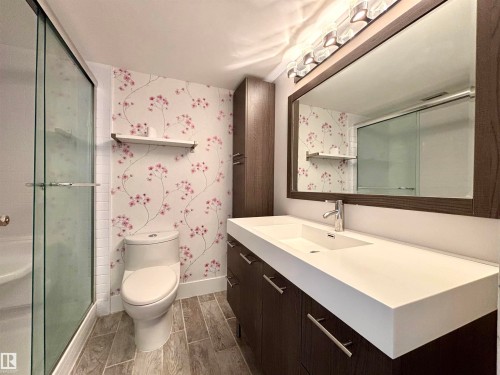 Full bathroom with wallpapered walls, vanity, a shower stall, and wood finish floors - 133 8735 165 Street, Edmonton, AB - Indoor Photo Showing Bathroom