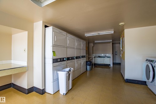 Community laundry featuring light flooring, stacked washer and clothes dryer, and washing machine and clothes dryer - 133 8735 165 Street, Edmonton, AB - Indoor Photo Showing Laundry Room