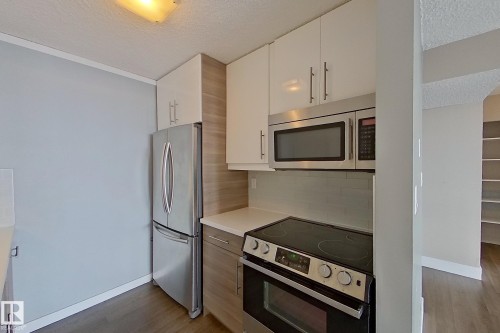 Kitchen with a textured ceiling, appliances with stainless steel finishes, light countertops, dark wood-style flooring, and white cabinets - 133 8735 165 Street, Edmonton, AB - Indoor Photo Showing Kitchen