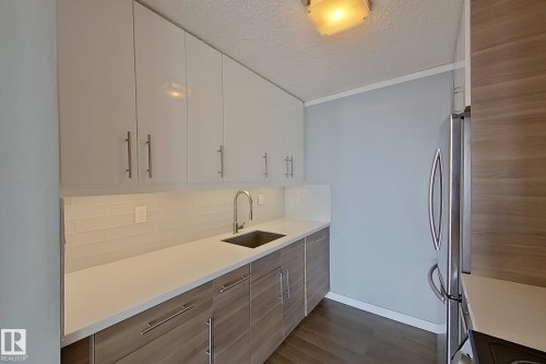 Kitchen with a textured ceiling, freestanding refrigerator, dark wood-style floors, white cabinetry, and modern cabinets - 133 8735 165 Street, Edmonton, AB - Indoor Photo Showing Kitchen