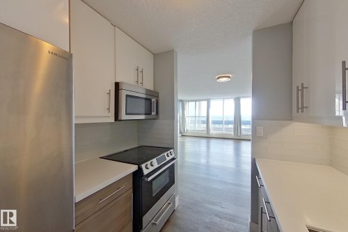 Kitchen with appliances with stainless steel finishes, a textured ceiling, tasteful backsplash, white cabinetry, and light wood-type flooring - 133 8735 165 Street, Edmonton, AB - Indoor Photo Showing Kitchen