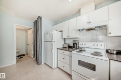 Kitchen with white appliances, dark countertops, under cabinet range hood, and white cabinetry - 