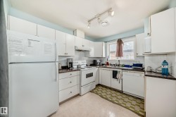Kitchen featuring dark countertops, white appliances, light floors, white cabinets, and under cabinet range hood - 