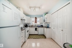 Kitchen featuring white appliances, light flooring, white cabinetry, dark countertops, and under cabinet range hood - 