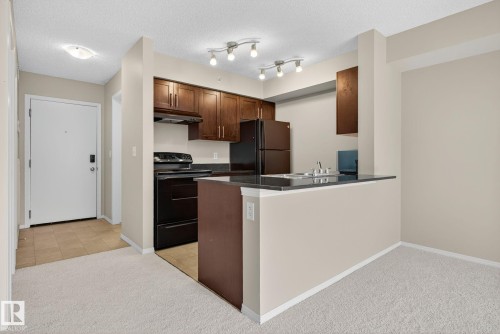 Kitchen with dark countertops, black appliances, light carpet, a textured ceiling, and a peninsula - 414 12035 22 Avenue, Edmonton, AB - Indoor Photo Showing Kitchen