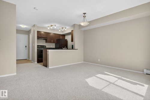 Kitchen featuring dark brown cabinets, pendant lighting, black appliances, open floor plan, and dark countertops - 414 12035 22 Avenue, Edmonton, AB - Indoor Photo Showing Kitchen