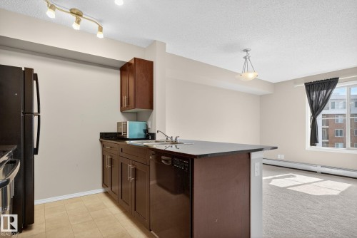 Kitchen with dark countertops, appliances with stainless steel finishes, a textured ceiling, hanging light fixtures, and a peninsula - 414 12035 22 Avenue, Edmonton, AB - Indoor Photo Showing Kitchen