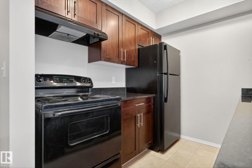 Kitchen featuring black appliances, ventilation hood, light tile patterned floors, dark stone countertops, and a textured ceiling - 414 12035 22 Avenue, Edmonton, AB - Indoor Photo Showing Kitchen