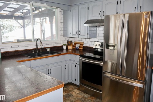 Kitchen with stainless steel appliances, dark countertops, white cabinets, under cabinet range hood, and stone finish floors - 4505 58 Avenue, Barrhead, AB - Indoor Photo Showing Kitchen With Double Sink