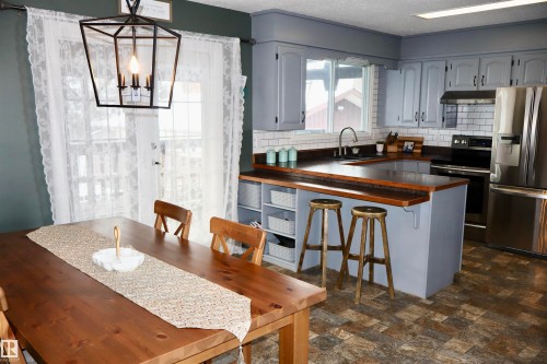 Kitchen with stainless steel appliances, a peninsula, decorative light fixtures, decorative backsplash, and a kitchen breakfast bar - 4505 58 Avenue, Barrhead, AB - Indoor