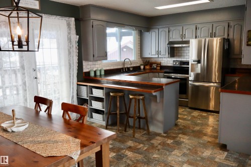Kitchen featuring dark countertops, appliances with stainless steel finishes, backsplash, stone finish flooring, and a peninsula - 4505 58 Avenue, Barrhead, AB - Indoor