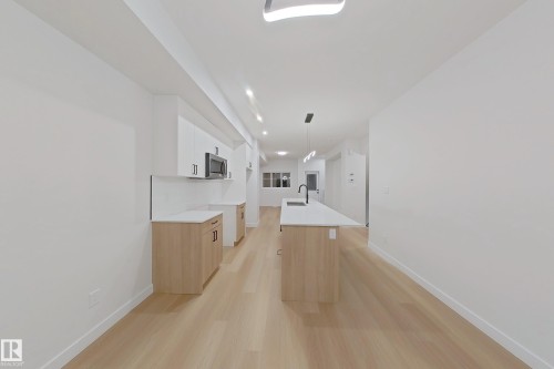 Kitchen featuring an island with sink, light wood-type flooring, decorative light fixtures, white cabinetry, and stainless steel microwave - 65 18120 28 Avenue, Edmonton, AB - Indoor Photo Showing Other Room