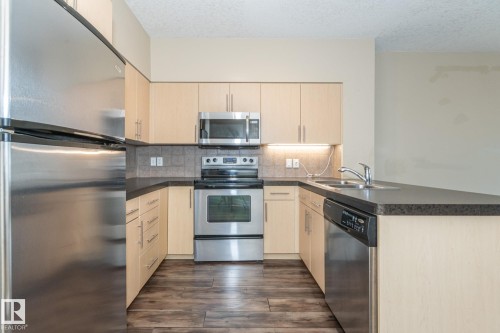 Kitchen featuring appliances with stainless steel finishes, a peninsula, decorative backsplash, light brown cabinets, and a textured ceiling - 904 10136 104 Street Nw, Edmonton, AB - Indoor Photo Showing Kitchen With Double Sink