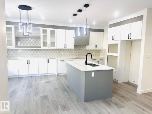 Kitchen with pendant lighting, glass fronted cabinets, a center island with sink, light wood-style flooring, and two tone cabinetry - 3906 41 Avenue, Beaumont, AB - Indoor Photo Showing Kitchen With Upgraded Kitchen