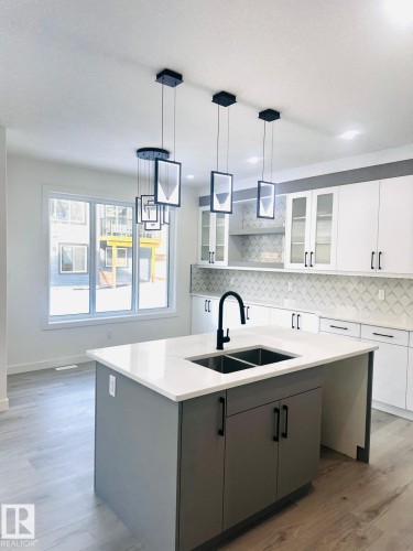Kitchen featuring two tone cabinets, decorative light fixtures, an island with sink, glass insert cabinets, and light wood-style floors - 3906 41 Avenue, Beaumont, AB - Indoor Photo Showing Kitchen With Double Sink With Upgraded Kitchen