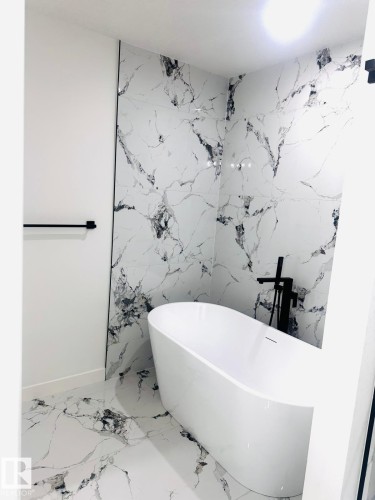 Full bathroom featuring a soaking tub, stone wall, and marble finish flooring - 3906 41 Avenue, Beaumont, AB -  Photo Showing Bathroom