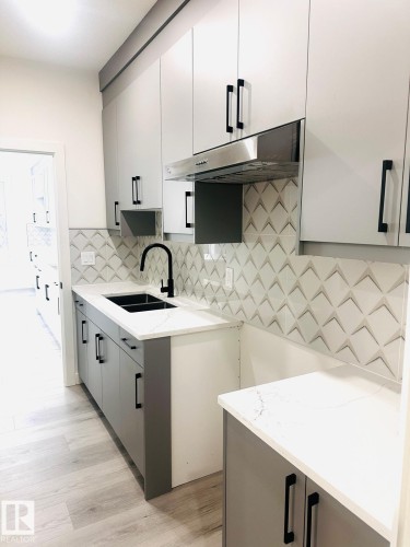 Kitchen featuring gray cabinetry, light wood finished floors, modern cabinets, light stone counters, and tasteful backsplash - 3906 41 Avenue, Beaumont, AB - Indoor Photo Showing Kitchen With Double Sink
