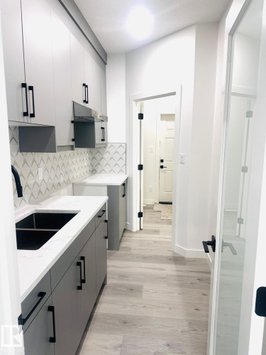 Kitchen with gray cabinetry, light wood-style floors, light stone counters, modern cabinets, and tasteful backsplash - 3906 41 Avenue, Beaumont, AB - Indoor Photo Showing Kitchen With Double Sink