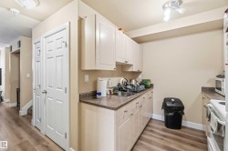 Kitchen with white appliances, light wood-style flooring, dark countertops, a textured ceiling, and white cabinetry - 