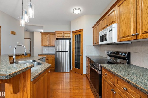 Kitchen with appliances with stainless steel finishes, decorative light fixtures, light wood finished floors, brown cabinets, and tasteful backsplash - 4931 48 Avenue, Onoway, AB - Indoor Photo Showing Kitchen With Double Sink