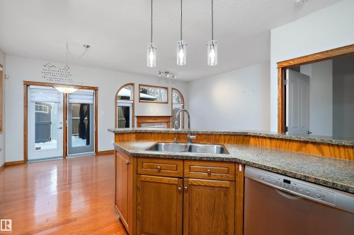 Kitchen with brown cabinetry, dishwasher, pendant lighting, light wood-type flooring, and a textured ceiling - 4931 48 Avenue, Onoway, AB - Indoor Photo Showing Kitchen With Double Sink