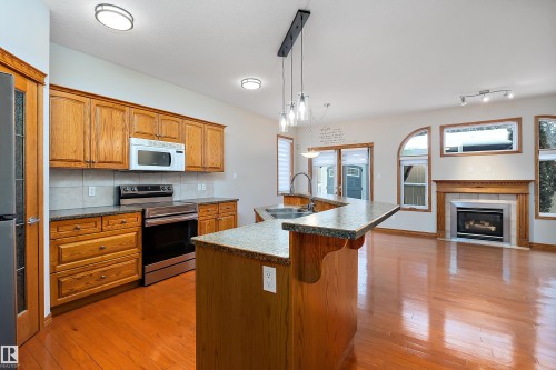 Kitchen featuring dark countertops, appliances with stainless steel finishes, pendant lighting, a center island with sink, and tasteful backsplash - 4931 48 Avenue, Onoway, AB - Indoor Photo Showing Kitchen With Fireplace With Double Sink