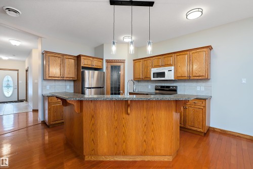 Kitchen with a breakfast bar area, appliances with stainless steel finishes, pendant lighting, tasteful backsplash, and brown cabinetry - 4931 48 Avenue, Onoway, AB - Indoor Photo Showing Kitchen