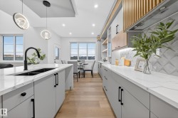Kitchen featuring light stone countertops, light wood-style floors, tasteful backsplash, white cabinets, and pendant lighting - 