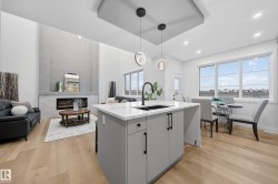 Kitchen with open floor plan, a kitchen island with sink, decorative light fixtures, a high end fireplace, and light stone counters - 