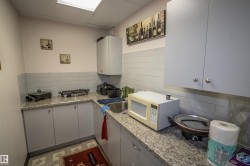 Kitchen with white microwave, backsplash, a drop ceiling, and light stone counters - 