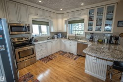 Kitchen with glass insert cabinets, stainless steel appliances, light stone counters, recessed lighting, and a breakfast bar area - 
