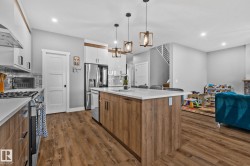 Kitchen featuring brown cabinets, appliances with stainless steel finishes, hanging light fixtures, white cabinets, and dark wood-type flooring - 