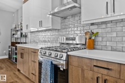 Kitchen featuring stainless steel gas range oven, wall chimney range hood, white cabinetry, modern cabinets, and backsplash - 